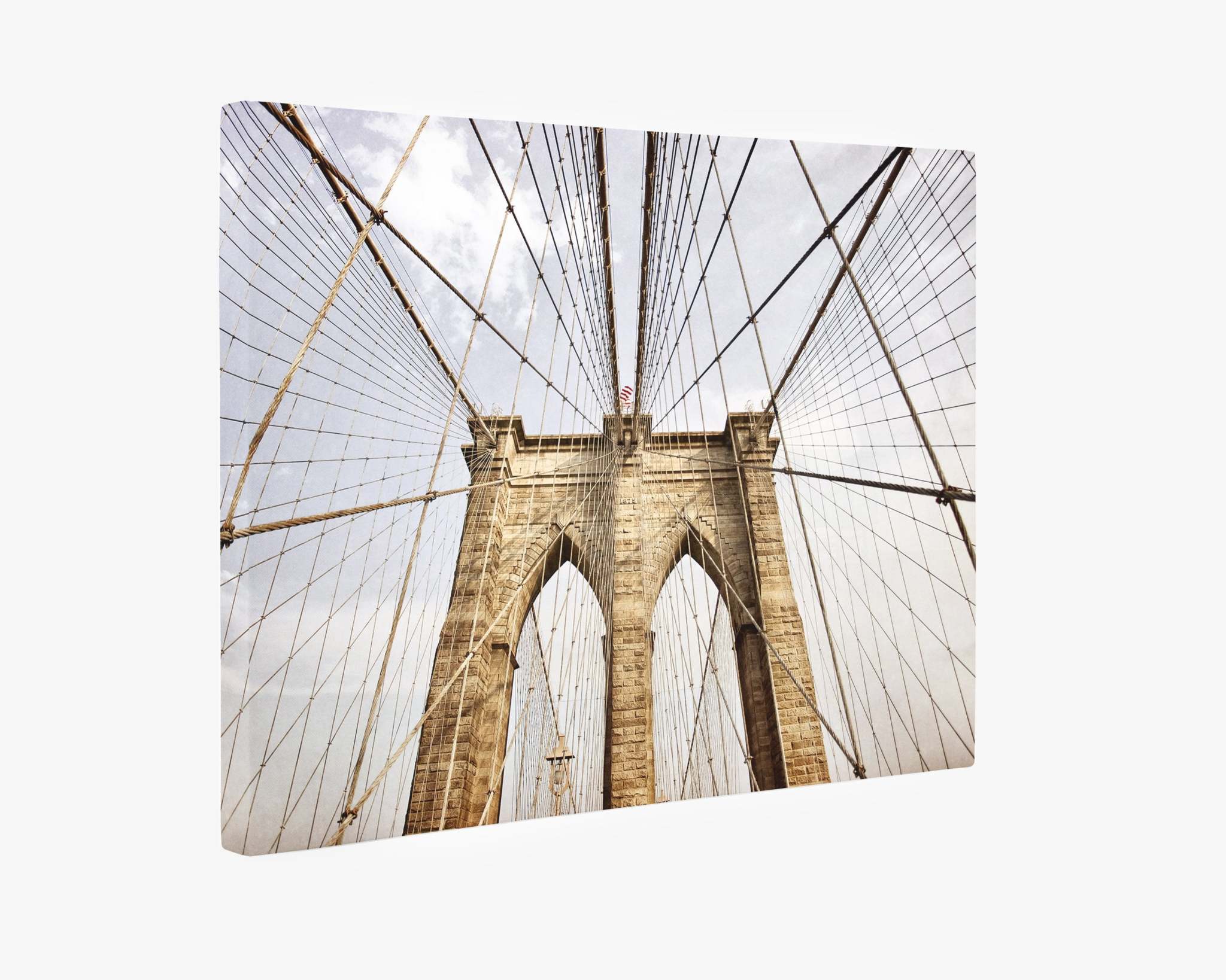 An Offley Green New York City Canvas Wall Art, &#39;Brooklyn Wires,&#39; featuring the iconic view of the Brooklyn Bridge. The image highlights the bridge&#39;s stone towers and intricate web of suspension cables against a cloudy sky backdrop. The perspective is upwards, emphasizing the architectural details and grandeur on premium artist-grade canvas.