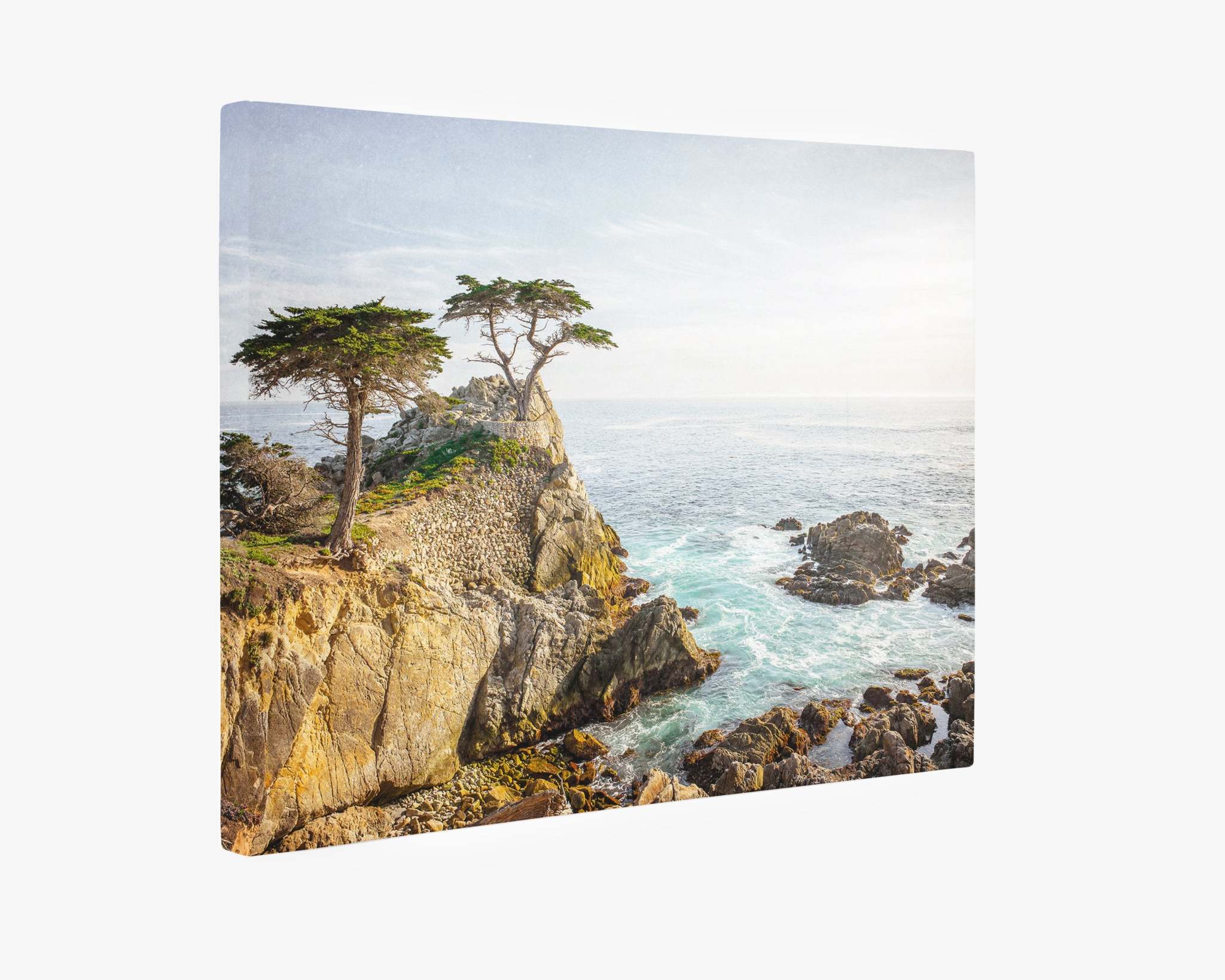 A canvas gallery wrap of a coastal scene featuring a rocky cliff with two lone trees atop it, surrounded by the ocean. The waves crash against the rocks under a partly cloudy sky, creating a serene and picturesque view. This piece embodies the beauty found in Offley Green's California Coastal Canvas Wall Art, 'Lone Cypress,' on premium artist-grade canvas.
